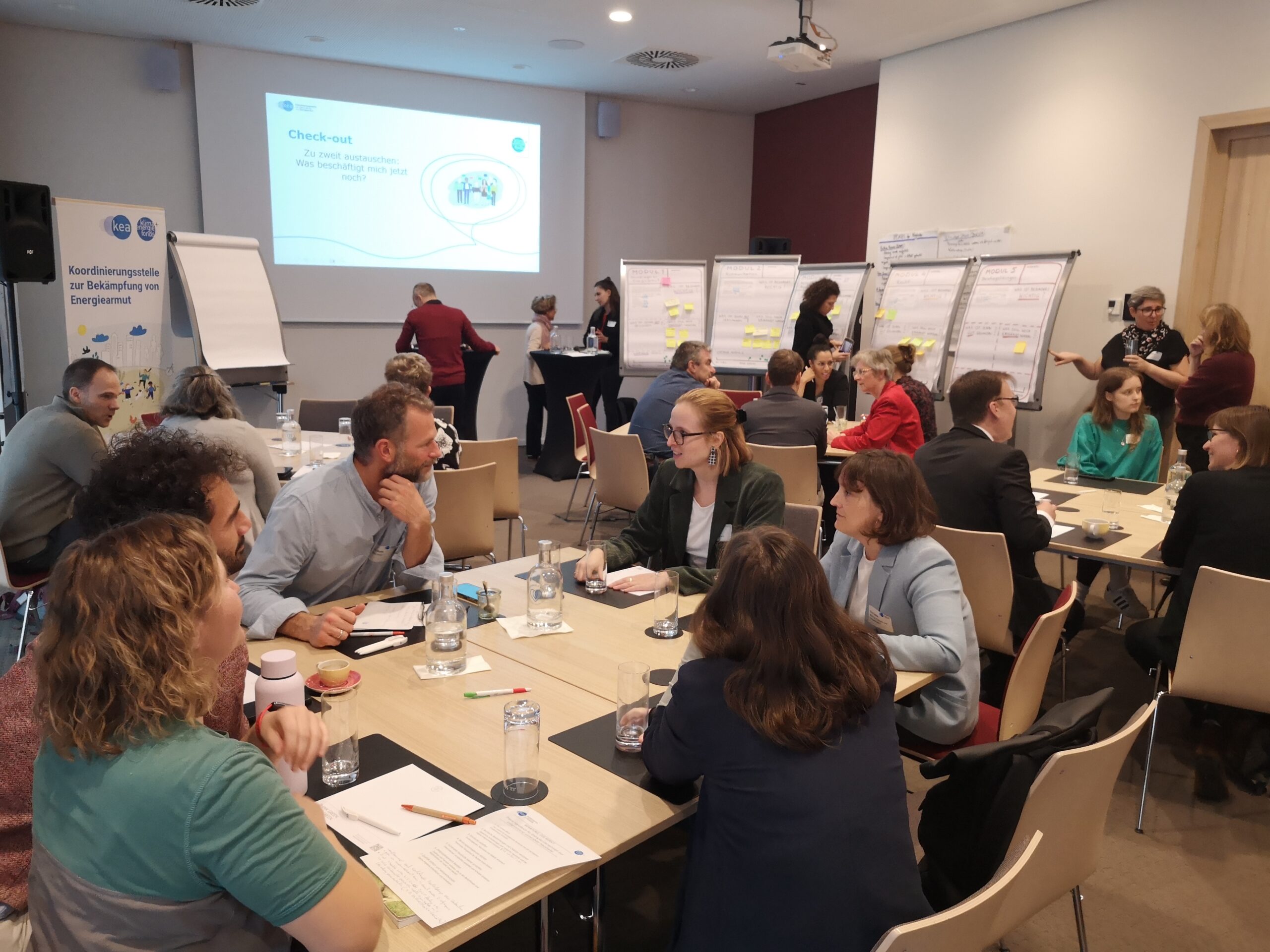 Teilnehmer:innen des 4. kea Forums zur Bekämpfung von Energiearmut sitzen um Tische herum und diskutieren.