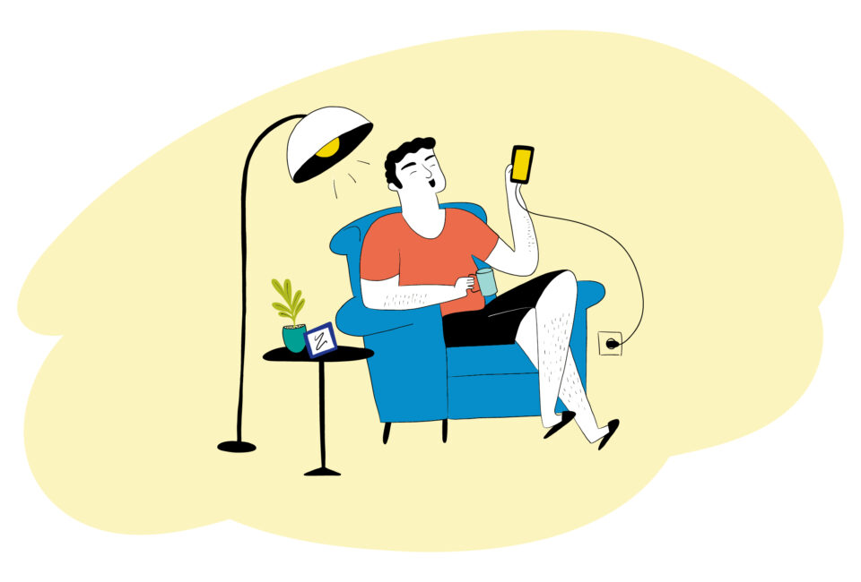 Eine Person sitzt auf einem Sessel und hält ein Smartphone in der Hand. Links von ihr leuchtet eine Stehlampe.